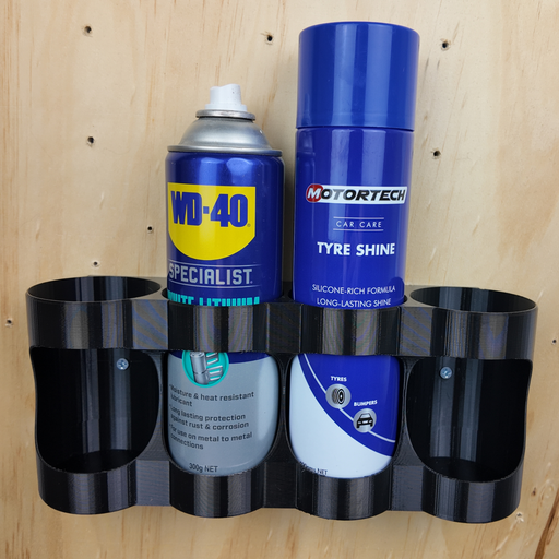 A black plastic 3-in-1 tire shine, tire lighting, and WD-40 can holder mounted on a light wood panel wall. The holder contains two blue aerosol cans: a WD-40 Specialist can on the left and a blue and white Motortech Tyre Shine can on the right.